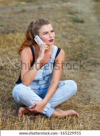 Beautiful pin-up girl in denim overalls and a T-shirt, with a cell phone in his hand on outdoors