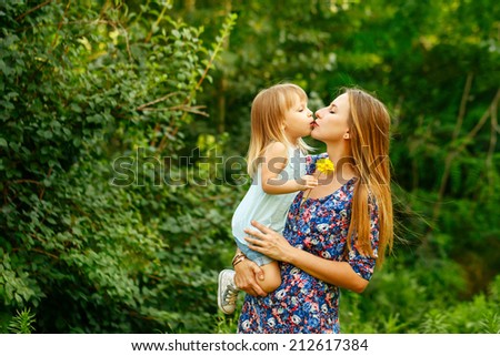 Mother and daughter on the walk in the city park. Mother hugs and kisses baby.