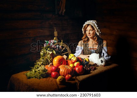Peasant Woman holding a rabbit. Table with vegetables and fruit stands next to a peasant.