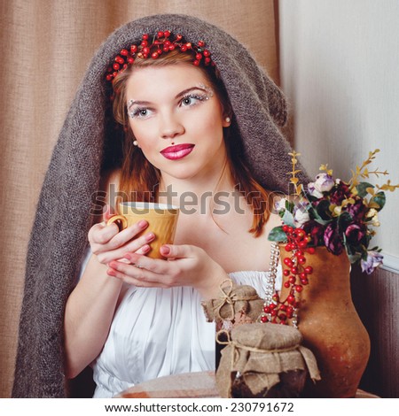 Young beautiful girl with an unusual make-up wearing a knitted scarf drinking hot tea