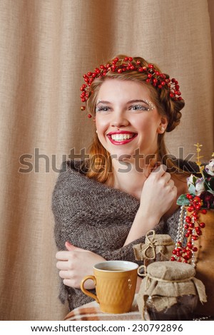 Young beautiful girl with an unusual make-up wearing a knitted scarf drinking hot tea
