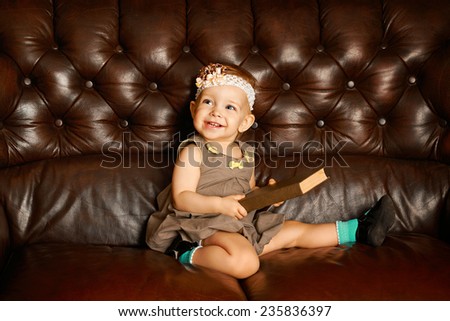 Little cute girl with big book sitting on a leather couch