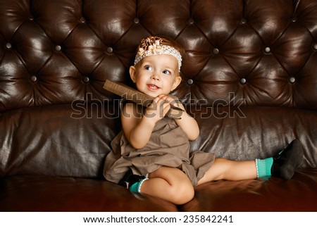 Little cute girl with big book sitting on a leather couch