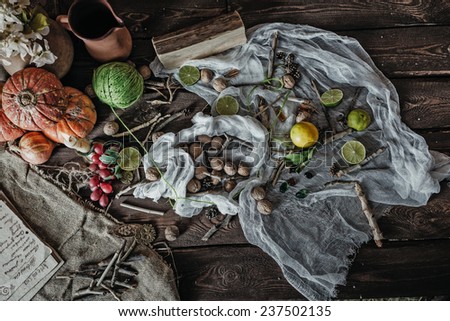 Still life of ingredients for making potions witch. Nuts, sticks, scrolls, thread, runes, charms, pumpkin, lime, lemon, pine cones and other ingredients lie on a wooden table.