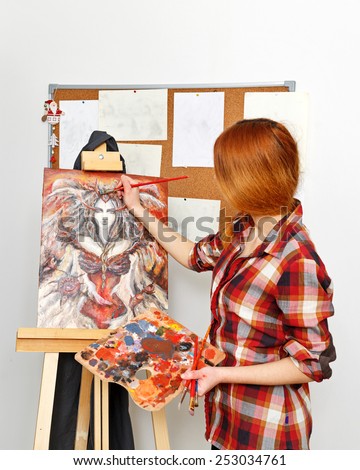 Young woman painting a picture on the canvas in his studio. The artist paints near an easel with a picture.