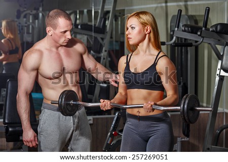 Coach with a client in the gym. Sports Man and athletic girl engaged in fitness in the gym. Trained with a barbell