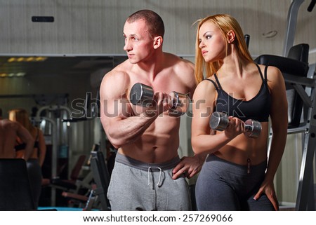 Coach with a client in the gym. Sports Man and athletic girl engaged in fitness in the gym. Train with dumbbells