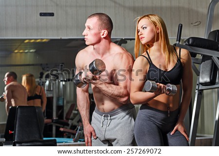 Coach with a client in the gym. Sports Man and athletic girl engaged in fitness in the gym. Train with dumbbells