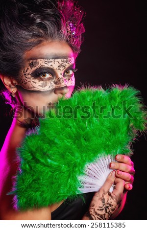 A mysterious young girl in masquerade mask holds in her hands a fan. Girl flirts.