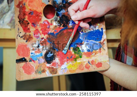 Artist brush mix color oil painting on palette is holding in his hand closeup
