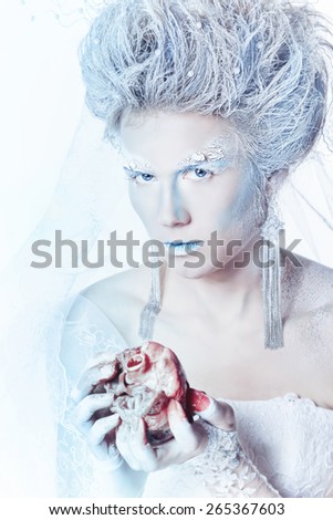 Mysterious and unusual girl with face art in the form of the Snow Queen. Girl holding a human heart in the blood. Bloodthirsty girl looking at the camera. The concept of eternal winter.
