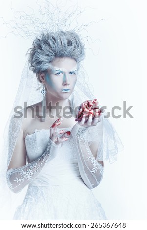 Mysterious and unusual girl with face art in the form of the Snow Queen. Girl holding a human heart in the blood. The girl closed her eyes. The concept of eternal winter.