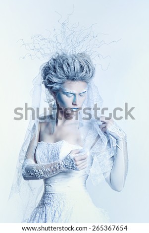 Mysterious and unusual girl with face art in the form of the Snow Queen. Girl dressed in a white dress and has a high hairstyle.