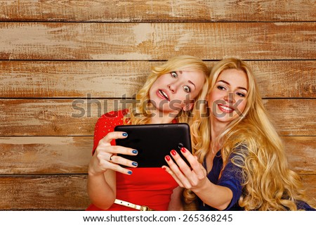 Young blonde sisters make fun group self, holding a tablet computer. Girls fool around communicating on the Internet. The concept of youth and technology.