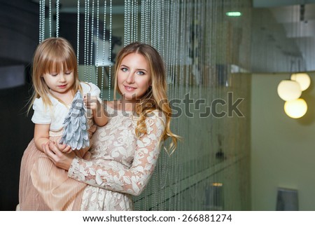 Young mother hugging her daughter tenderly. Mother holds daughter on hands. Daughter holds the mock of the Christmas tree. The concept of family happiness.