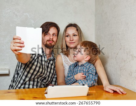 Young family. Mother, father and son are doing self sitting at the kitchen table. Social network. Happy childhood.