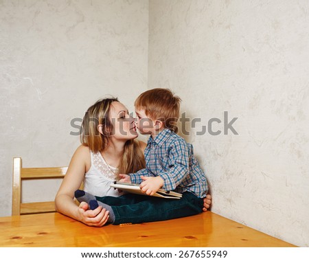 Mother and child play on a Tablet PC in the kitchen. Family leisure, modern, young and technology. Boy holding a tablet, and the mother of his kisses.