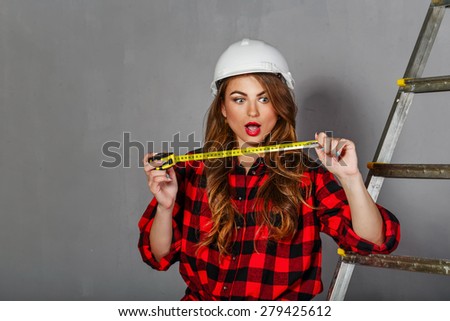 Young girl construction worker holding tape measure. Woman showing emotion of surprise. Girl dressed in jeans, plaid shirt and helmet. Concept of building and architecture.