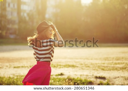 Portrait of a girl in a hat walking in a city park. Shooting at sunset. Sun glare in the frame. Walk. The concept of street fashion.