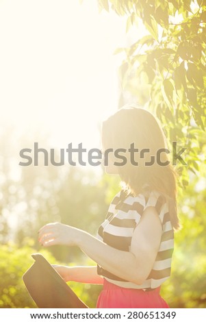 Young attractive girl in a hat and fashionable dress. Shooting at sunset in city park. Sun glare in the frame. The concept of street fashion.