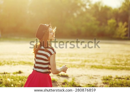 Portrait of a girl in a hat walking in a city park. Shooting in the sunset from the back. Sun glare in the frame. Walk. The concept of street fashion.
