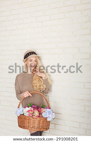 Attractive woman dressed in a sweater and cap holding a basket of flowers. The concept of innocent beauty.