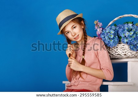 Cute teen girl basket of flowers. The girl smiles. At the head of the girl a hat. The concept of children living flowers.