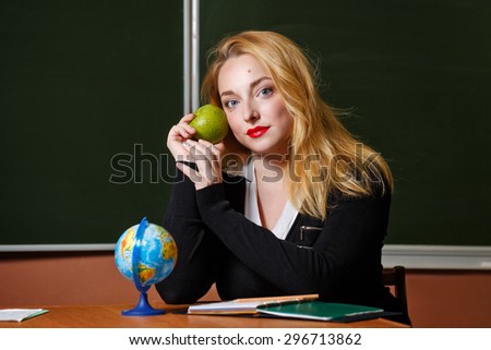 Geography teacher sitting at her desk. A girl holding a green apple. Back to school.