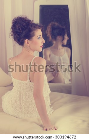 Young sexy girl sits in front of the mirror in her bedroom. The reflection in the mirror. Boudoir fashion.