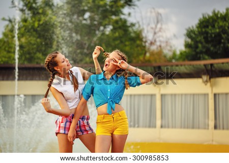 Teen girl straightens hairstyle\'s best friend at the fountain in summer park. Girls dressed in shorts and a shirt. On summer vacation. The concept of true friendship.