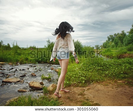 Young carefree boho girl went off along the river bank. Stylish lifestyle portrait.