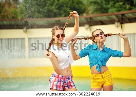 Teen girl in sunglasses have fun near the fountain in summer park. Girls dressed in shorts and a shirt. On summer vacation. The concept of true friendship.