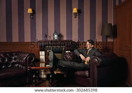 Successful businessman relaxing with his feet up on the coffee table, sitting in a leather armchair manager. Vintage background. Leadership concept.
