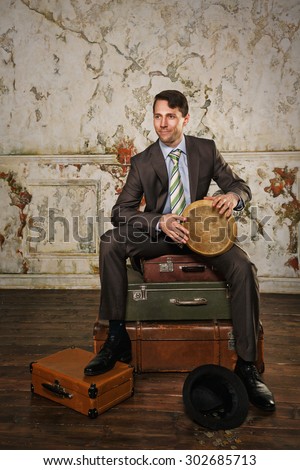 Businessman sitting on suitcases. The man playing the bongos collecting money for a new project. A hat with coins lying at his feet. Business trip. Vintage background. The concept of a startup.