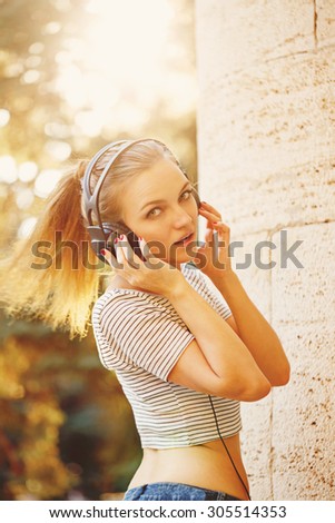 Young hipster girl listening to music on headphones at sunset. The concept of youth culture. Soft focus