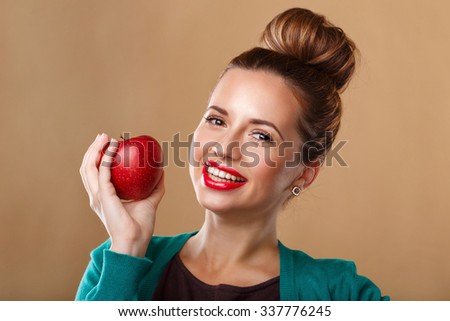 Portrait of girl with clear skin holding an apple. Girl smiles and shows beautiful, even white teeth. Makeup underlines the beautiful facial features of the model. Red lipstick.