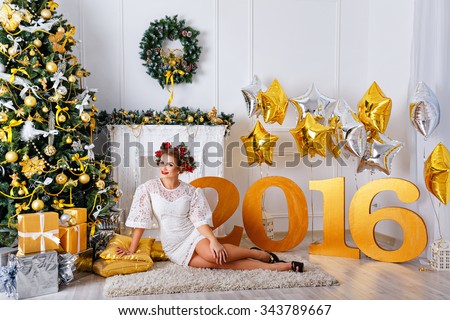 A girl sitting on the carpet next to the Christmas tree and presents. The meeting of New Year 2016. Christmas hairstyle.