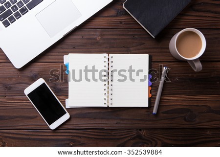 Top view office desk mockup: laptop, notebook, smartphone, and cup of coffee on rustic brown wooden background