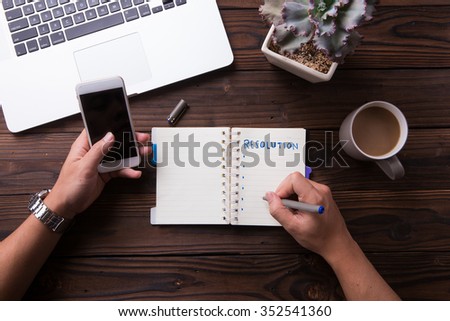 Top view office desk mockup: laptop, notebook, smartphone, flower plant, and cup of coffee on rustic brown wooden background. New year resolution 2016