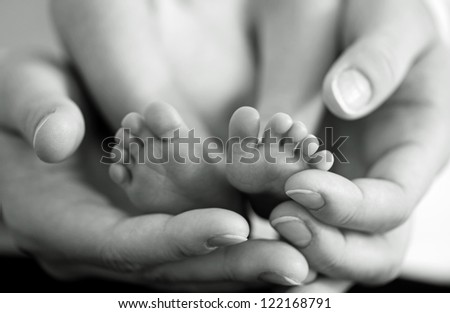 Mother gently hold baby leg in hand. Black and white image with soft focus on babie\'s foot
