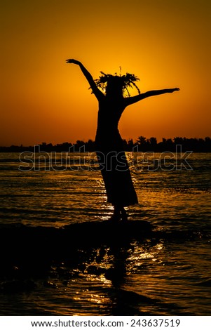 Young girl in a wreath dancing at sunrise (sunset) on the banks of the river.