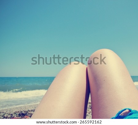 Legs of a young woman lying on the beach, on a sunny summer day. Filtered image in faded, washed-out, retro style; can be used as a background.