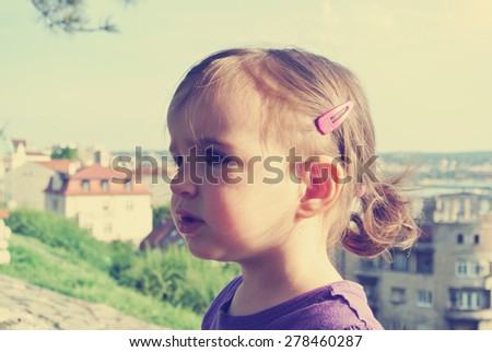 Portrait of a little dark haired girl with pony tail, on a sunny day. Image filtered in faded, washed out, retro, vintage style.