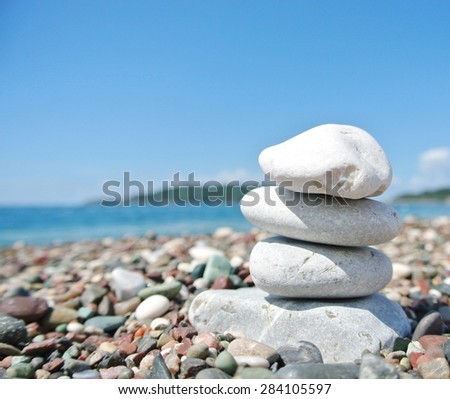 Stack of white stones balancing on the pebbly beach, on a sunny day, with sea in the background. Concept of balance, peace, harmony, well-being, and zen.