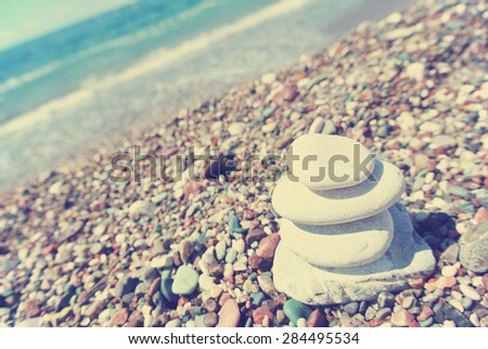 Stack of white stones balancing on the pebbly beach. Image filtered in faded, washed out, retro style; summer vintage concept. Concept of balance, harmony and well-being. Tilted perspective.