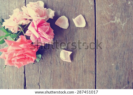 Romantic background - rustic wooden table with pink roses and rose petals. Image filtered in faded, washed out, retro style; romantic vintage concept.