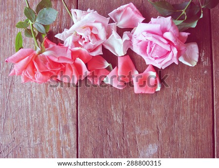 Romantic background - rustic wooden table with pink roses and rose petals. Image edited in faded, washed out, retro effect with red instagram style filter; romantic vintage concept.