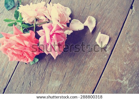 Romantic background - rustic wooden table with pink roses and rose petals. Image filtered in faded, washed out, retro style; romantic vintage concept.