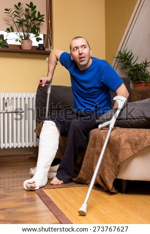 A man with a broken leg tries to stand up on crutches from a couch