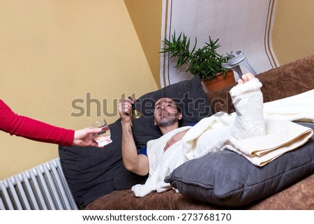 A man with a broken leg is lying on a couch and is being served